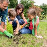 Cheerful family planting tree together in their backyard garden