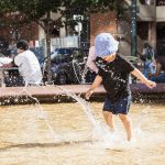 Little boy jumping in fountain on a hot summer day